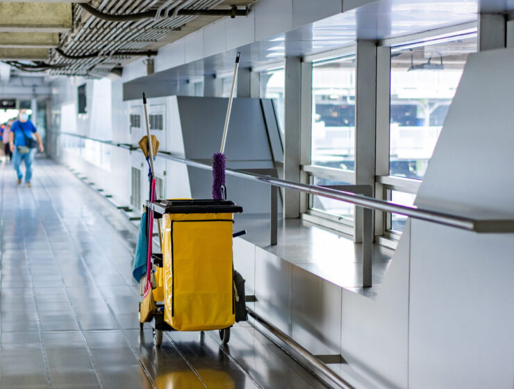 Cleaning equipment of housekeeper by mobs, bins, wipes and brooms in hall at the airport with blurry people background.