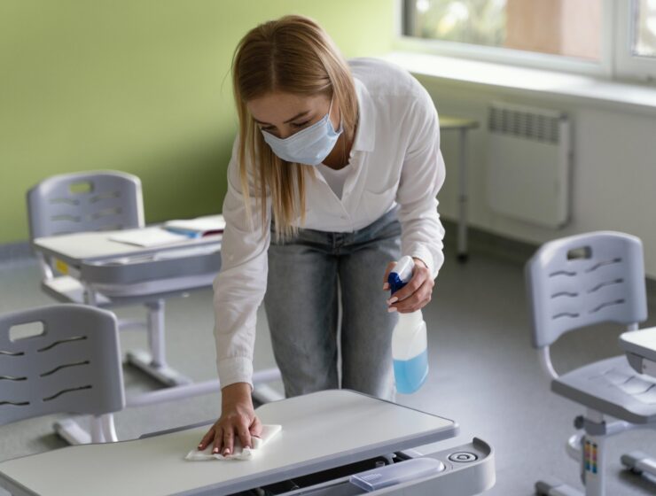 female-teacher-disinfecting-school-benches-classroom