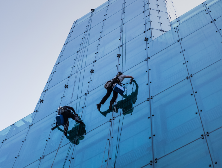 vertical-low-angle-shot-two-people-climbing-tall-glass-building-day-time.webp