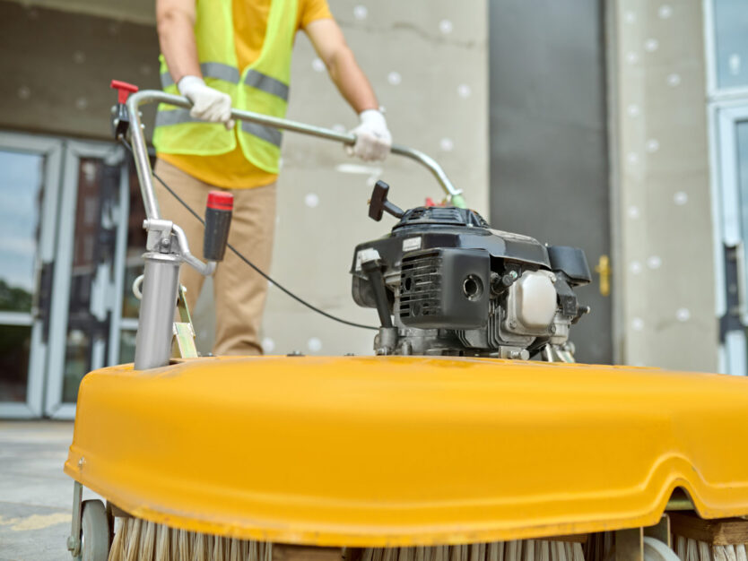 Workman applying a road sweeper on the construction site Cropped photo of a worker cleaning the outdoor floor tiles with a street sweeping machine