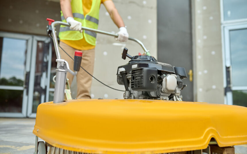 Workman applying a road sweeper on the construction site Cropped photo of a worker cleaning the outdoor floor tiles with a street sweeping machine